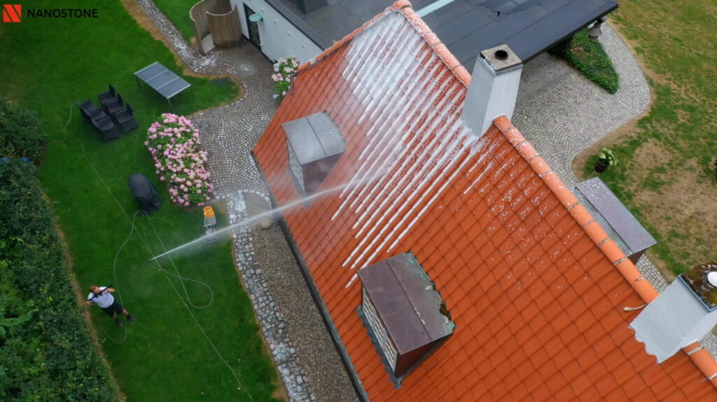 Drone billede af en Nanostone medarbejder der påføre algebehandling på et rødt tegltag med en lanse
