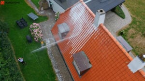 Drone billede af en Nanostone medarbejder der påføre algebehandling på et rødt tegltag med en lanse