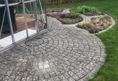 Rund brostensbelagt terrasse med bede ved vinterhave i Solrød før rensning